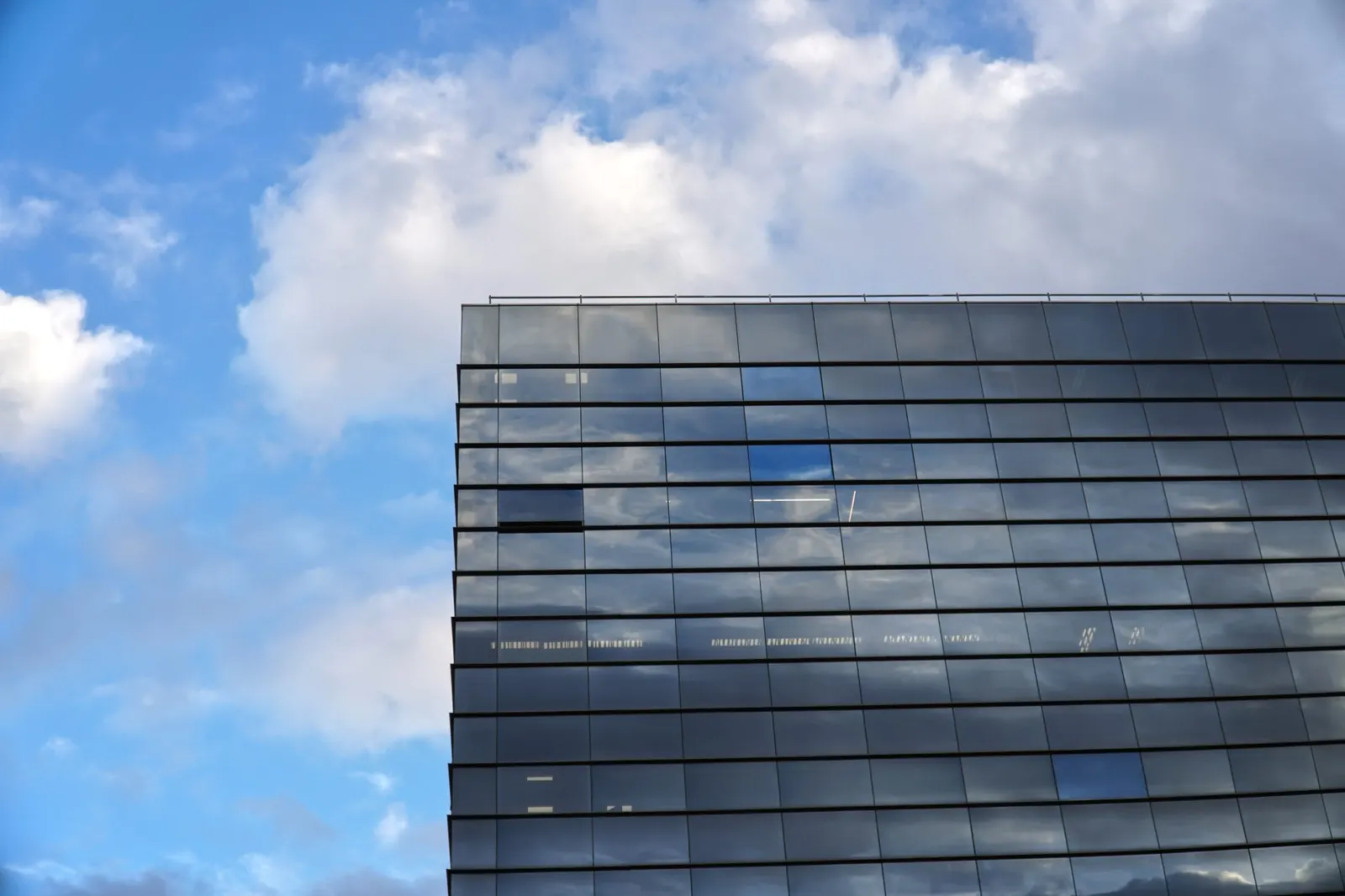 Glasfassade eines modernen Bürogebäudes vor blauem Himmel mit Wolken