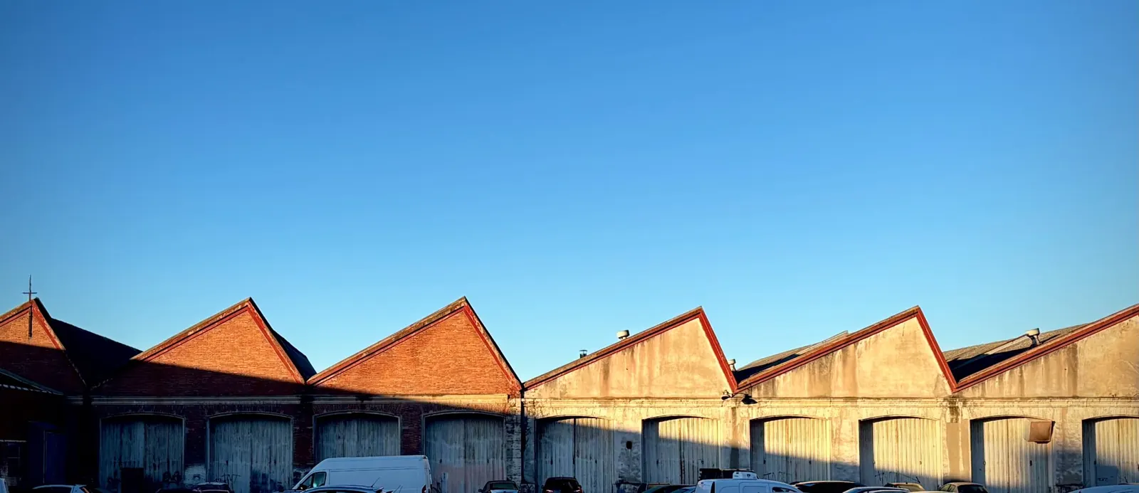 Reihe von Gewerbehallen mit Sheddächern vor klarem blauem Himmel