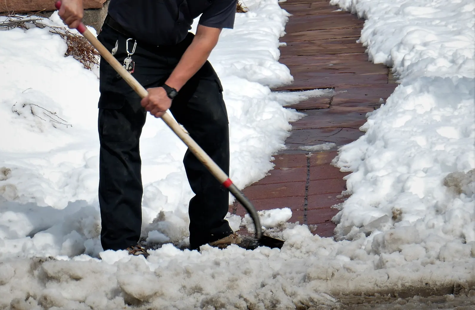 Arbeiter räumt mit einer Schneeschaufel Schnee von einem gepflasterten Gehweg